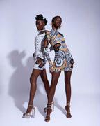 Two women wearing patterned outfits standing back-to-back against a white background